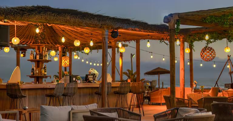 Bar en plein air à la tombée de la nuit, guirlandes lumineuses et toit de chaume
