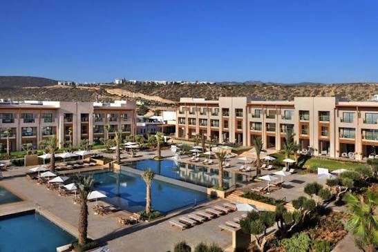 Vue d'ensemble d'un complexe hôtelier avec piscines et jardins, montagnes en arrière-plan